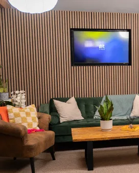The Unit Studio lounge, with a green velvet sofa and armchair in front of a slatted wood wall and a wall-mounted screen
