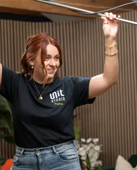 Unit Studio team member smiling while adjusting an overhead lighting rig in the studio