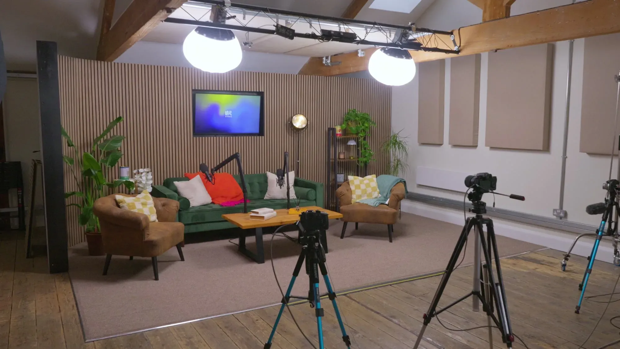 An interior shot of Unit Studio, in the foreground is a comfy chair. In the middle of the shot is a production suite, computer and monitors, then in the background a large glass enclosed studio